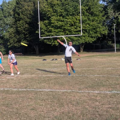 Players running for a disc on an outdoor pitch, backlit by low evening sun