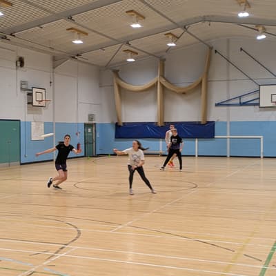 Players chasing down a low disc during an indoor session in a sports hall
